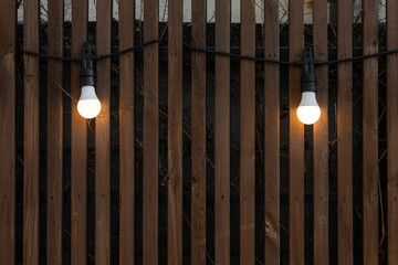 Warm lights garland bulbs hanging on brown wood pattern wall.