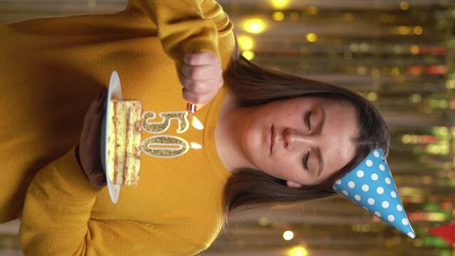 Beautiful happy young woman wearing sweater holding birthday cake number 50 golden candles burning by lighter. Concept of celebrating birthday and anniversary. POV.