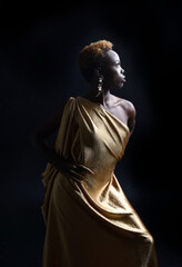  fantasy portrait of beautiful african woman model with afro, goddess silk robes and ornate floral wreath crown. gestural Posing holding golden flowers. isolated on dark  studio background 