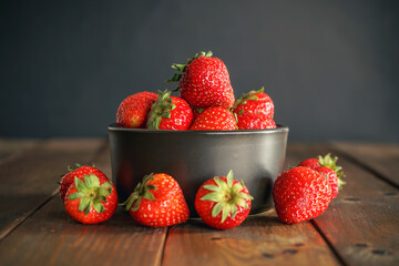 Strawberries in a black ceramic bowl on a wooden table with selective focus