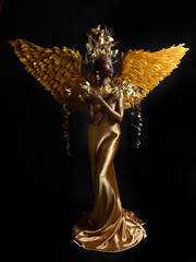  fantasy portrait of beautiful african woman model with afro, goddess silk robes, ornate crown & gold angel wings.  gestural Posing holding golden flowers., isolated on dark  studio background 