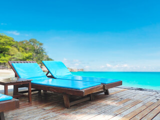 Wooden blue sun bed on wood floor over beach against blue sky.