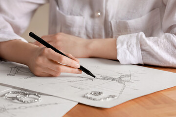 Naklejka premium Jeweler drawing sketch of elegant necklace on paper at wooden table, closeup