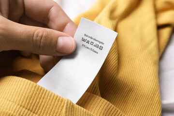 Woman holding clothing label on yellow garment, closeup