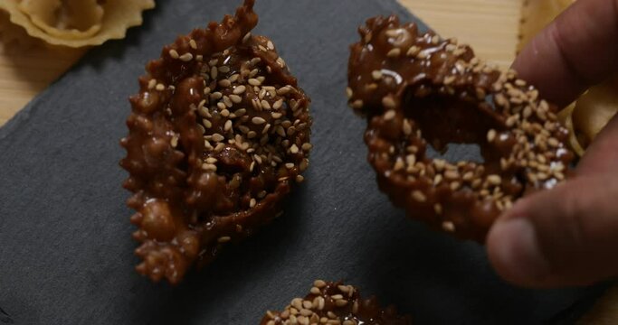 Indulge in the sensory delight of Chebakia, a cherished Moroccan pastry, through this close-up footage. Witness the intricate texture and flavors as the hand delicately presents the twisted pieces on 