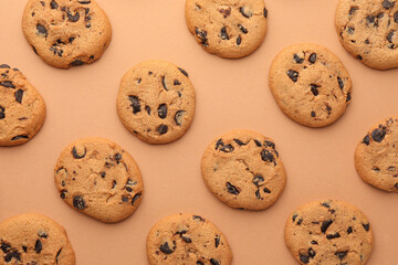 Many delicious chocolate chip cookies on beige background, flat lay