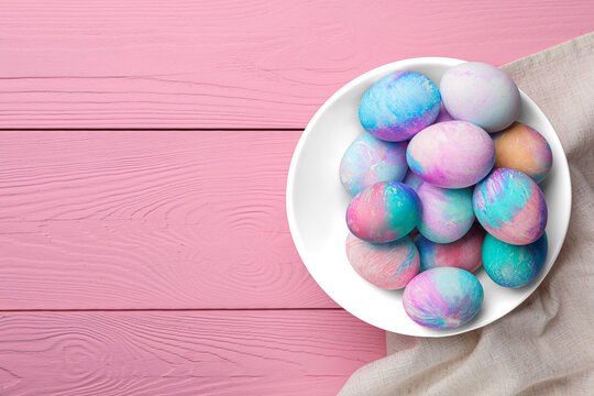 Bowl of decorated easter eggs on pink wooden table. top view. Space for text
