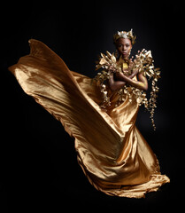 fantasy portrait of beautiful african woman model with afro, goddess silk robes and ornate floral wreath crown. gestural Posing holding golden flowers. isolated on dark  studio background 