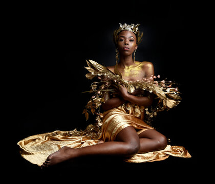  fantasy portrait of beautiful african woman model with afro, goddess silk robes and ornate floral wreath crown. gestural Posing holding golden flowers. isolated on dark  studio background 