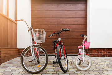 Family Bikes Riding concept. Children Bikes and Adult Bicycle under House Garage Door. Bicycles for...
