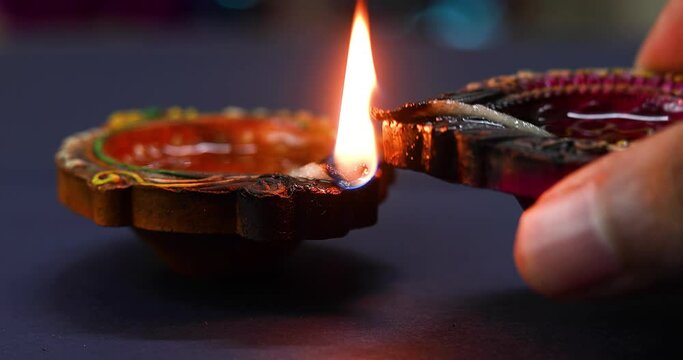 A woman's hand on a burning oil lamp lights another oil lamp. Close-up view