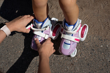 Close-up Mom putting on inline skates rollers to daughter child in public park in summer. Family...
