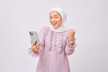 Excited beautiful young Asian Muslim woman wearing hijab and purple dress  using mobile phone and...