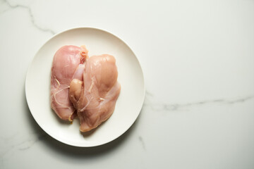 Two raw chicken fillets or chicken breasts on white plate. White and clean marble background. Ready to prepare and cooking. Healthy and low fat ingredient. Copy space. Top view. 
