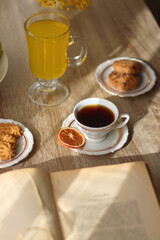 Cup of tea, plates with cookies, glass of orange juice, books, reading glasses, bowl of fruit and candles on the table. Selective focus.