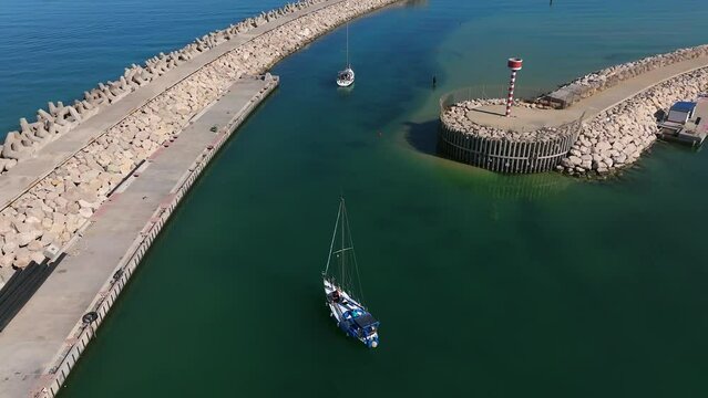 Aerial view of a Small sail boat leaving a marina slowly 