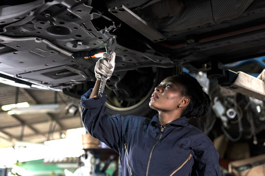 Black car mechanic woman using wrench reparing underneath vehicle in auto repair shop, Car Mechanic Concept