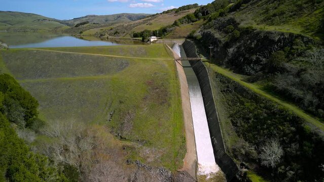 Water flows down spillway at Nicasio Reservoir in green California landscape