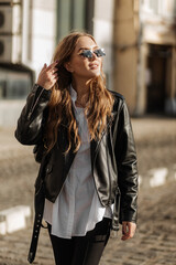 Obraz premium Fashionable blonde woman model with black leather jacket and style sunglasses walking the city street