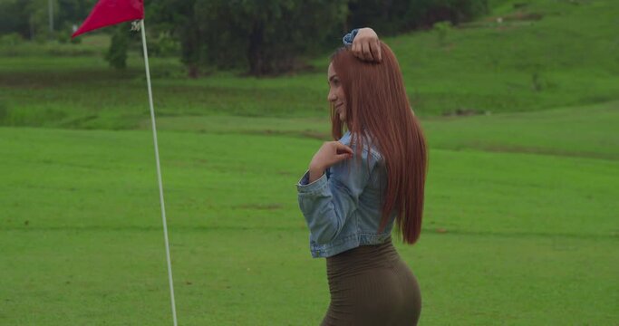 Latina woman in a short green dress standing on a golf course on a cloudy day