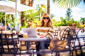 Attractive woman with toothy smile sitting at outdoor cafe and using laptop for work