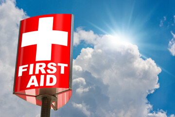 Close-up of a modern red and white First Aid Sign against a clear blue sky with clouds and sunbeams. Photography.
