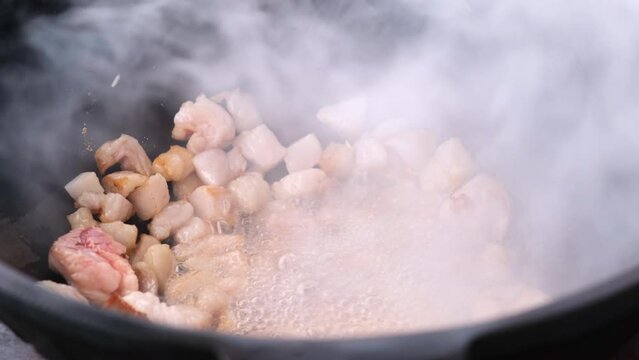 Close-up of the beginning of cooking delicious pilaf in a large cast-iron cauldron, frying fat tail on an open fire. Cooking at the street fair, folk cuisine festival. 