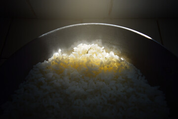 A ray of sunlight illuminates the end of an old iron skillet filled with rice in an unlit place....