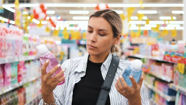 Attractive Young Mixed Race Woman Choosing Eco Vegan Natural Organic Shampoo from Two Different Bottles at Cosmetics in Supermarket, High Quality 4K Slow Motion Conscious Consumption Shopping Concept.