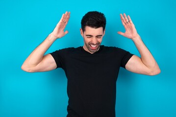 Young man standing over blue studio background goes crazy as head goes around feels stressed because of horrible situation