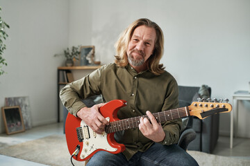 Portrait of mature guitarist with long hair looking at camera while playing guitar online