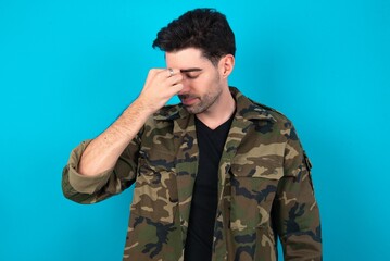 Fototapeta premium Sad Young man standing over blue studio background suffering from headache holding hand on her face