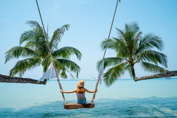 Asian woman relaxing on a wooden swing under the shade of palm trees. concept of nature tourism