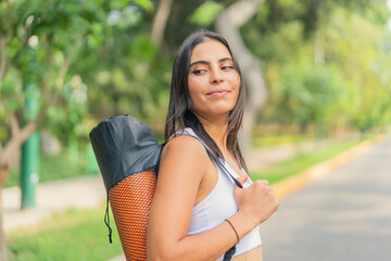 Young athletic woman carrying her yoga mat while walking in the park.