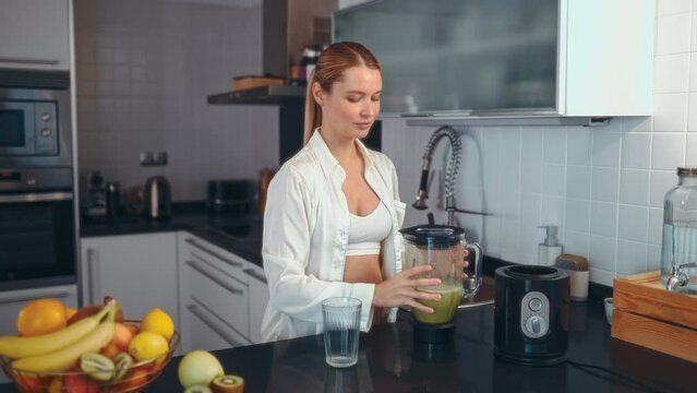 A young pregnant woman is preparing a smoothie with a blender in the kitchen. A pregnant woman drinks a vitamin smoothie. The concept of healthy eating during pregnancy.