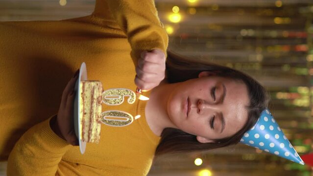 Beautiful happy young woman wearing sweater holding birthday cake number 60 golden candles burning by lighter. Concept of celebrating birthday and anniversary. POV.