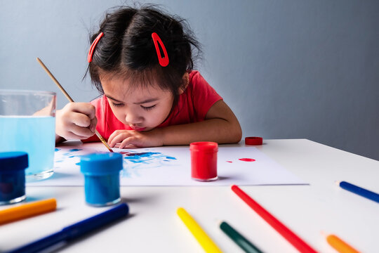 Asian kid learning with using brush painting on empty sheet of white paper