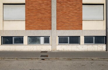 Condominium facade at the roadside with basement windows below and shutters. Tiled sidewalk and...
