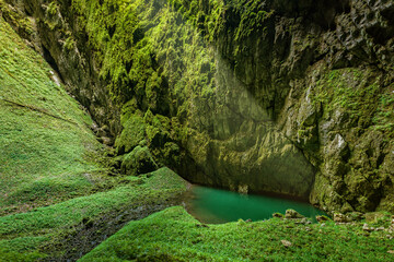 shady steep gorge with a lake and an entrance to a cave complex Macocha