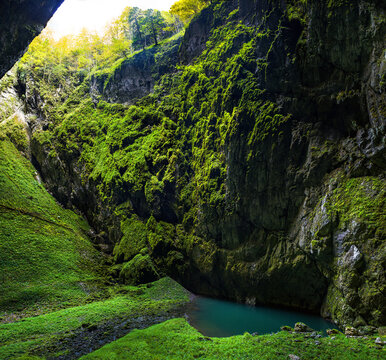 shady steep gorge with a lake and an entrance to a cave complex Macocha