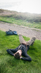 Hombre barbudo tumbado en pradera de hierba junto a mochila de senderista