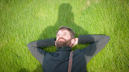 Hombre barbudo tumbado en pradera de hierba y sombra de fotografo encima