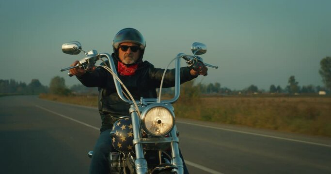 Portrait of Active Senior Retired Motorcyclist with Protective Helmet and Leather Jacket Riding his Custom Motorbike with American Flag Paint. Middle-Aged Man Enjoying his Freedom, Doing a Road Trip