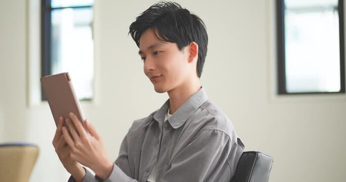 ソファでコーヒーを飲みながらタブレットを見る若い男性