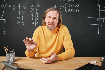 Portrait of teacher looking at camera and explaining topic in the classroom against blackboard