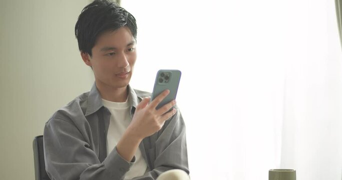 ソファに座ってスマートフォンを操作する若い男性