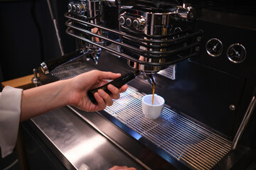 A waitress preparing coffee on coffee machine in cafeteria.