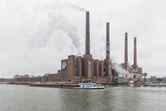 Wolfsburg, Germany – March 9, 2023: Power plant of Volkswagen factory on Mittelland Canal., cargo ship passing by