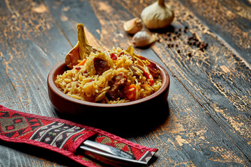 Classic pilaf with beef, garlic and carrots in a clay plate on a wooden background. Rustic