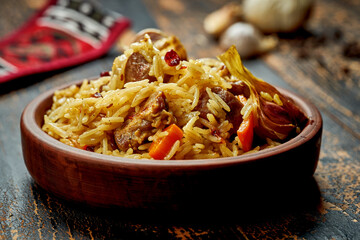 Classic pilaf with beef, garlic and carrots in a clay plate on a wooden background. Rustic